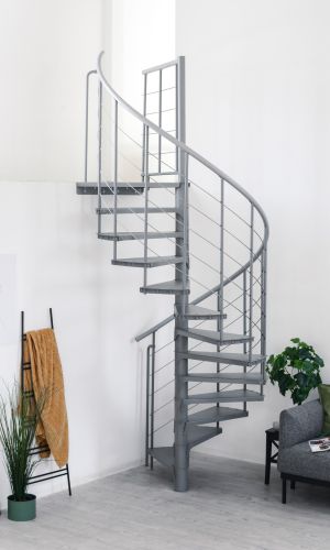 Spiral staircase Spino Smart in grey metal in a modern living space. The winding stairs lead upwards, the railing consists of vertical rods and stainless steel cables. In the background are a sofa, plants, and decorations.