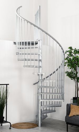 Outdoor spiral staircase Rondo Zink Smart made of galvanized metal in a modern living space. The spiral staircase leads upwards, with plants, a rug and a grey sofa with cushions in the foreground.