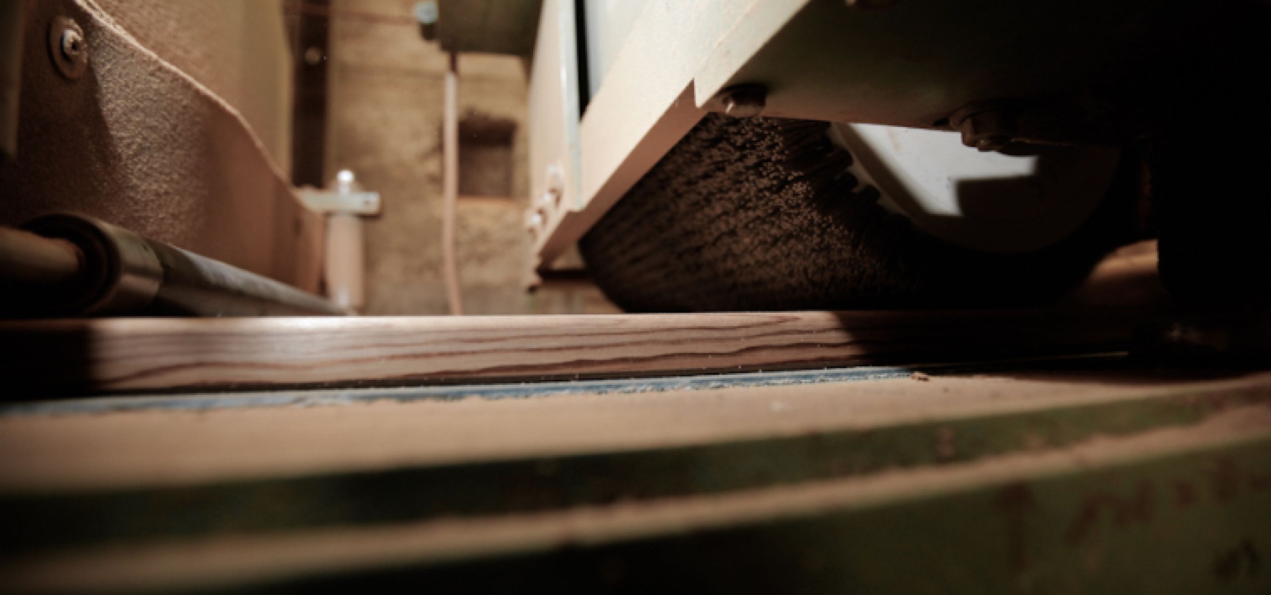 Wooden board being processed under a machine with a rotating brush – brushing treatment of wood surface.