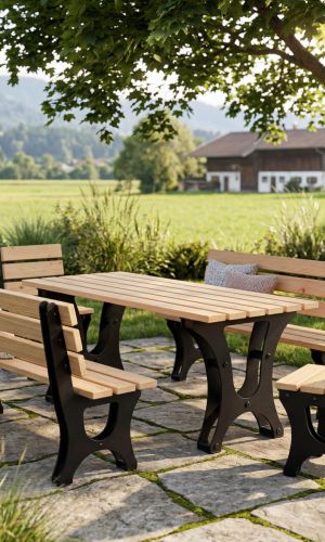 Campo garden dining set with a solid wooden table, two matching benches and one chair featuring black powder-coated steel frames, placed on a stone patio beneath a large tree with a scenic countryside and mountain landscape in the background.