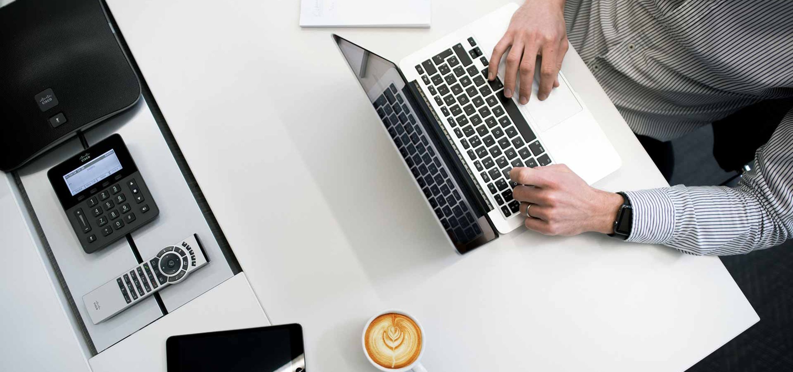 Man sitting at a white desk and typing something on a laptop