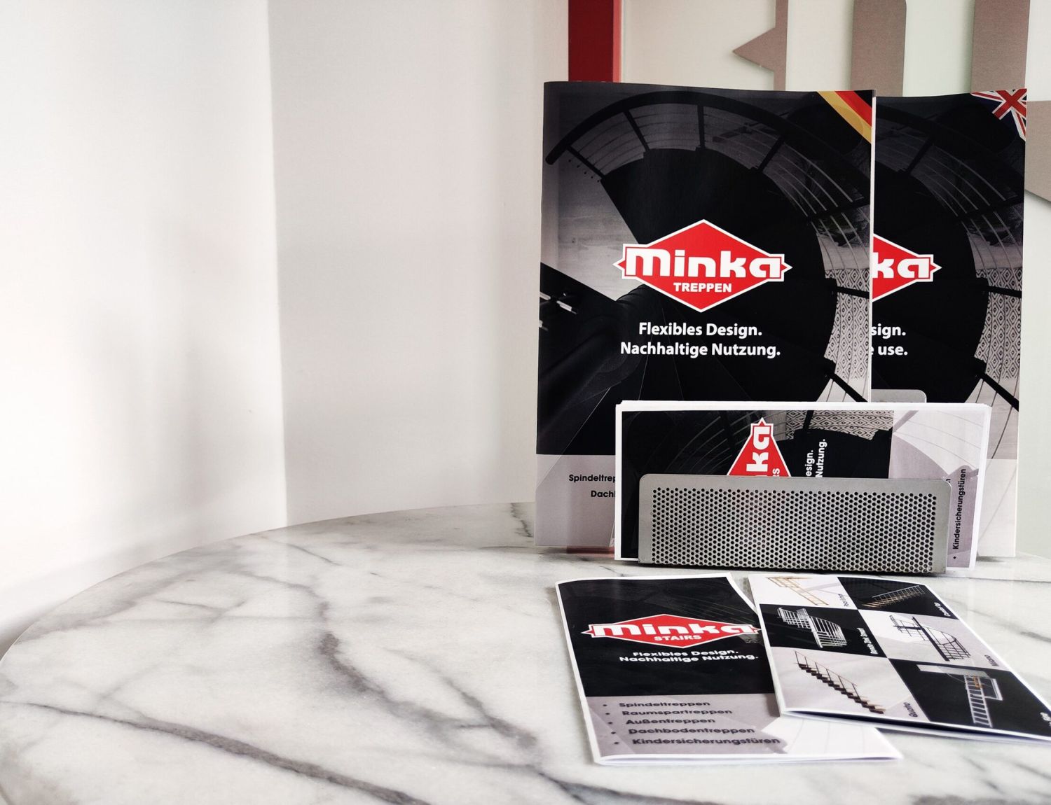 Downloads: Verschiedene Informationsmaterialien und Broschüren der Firma Minka Treppen auf einem runden Marmortisch ausgelegt.