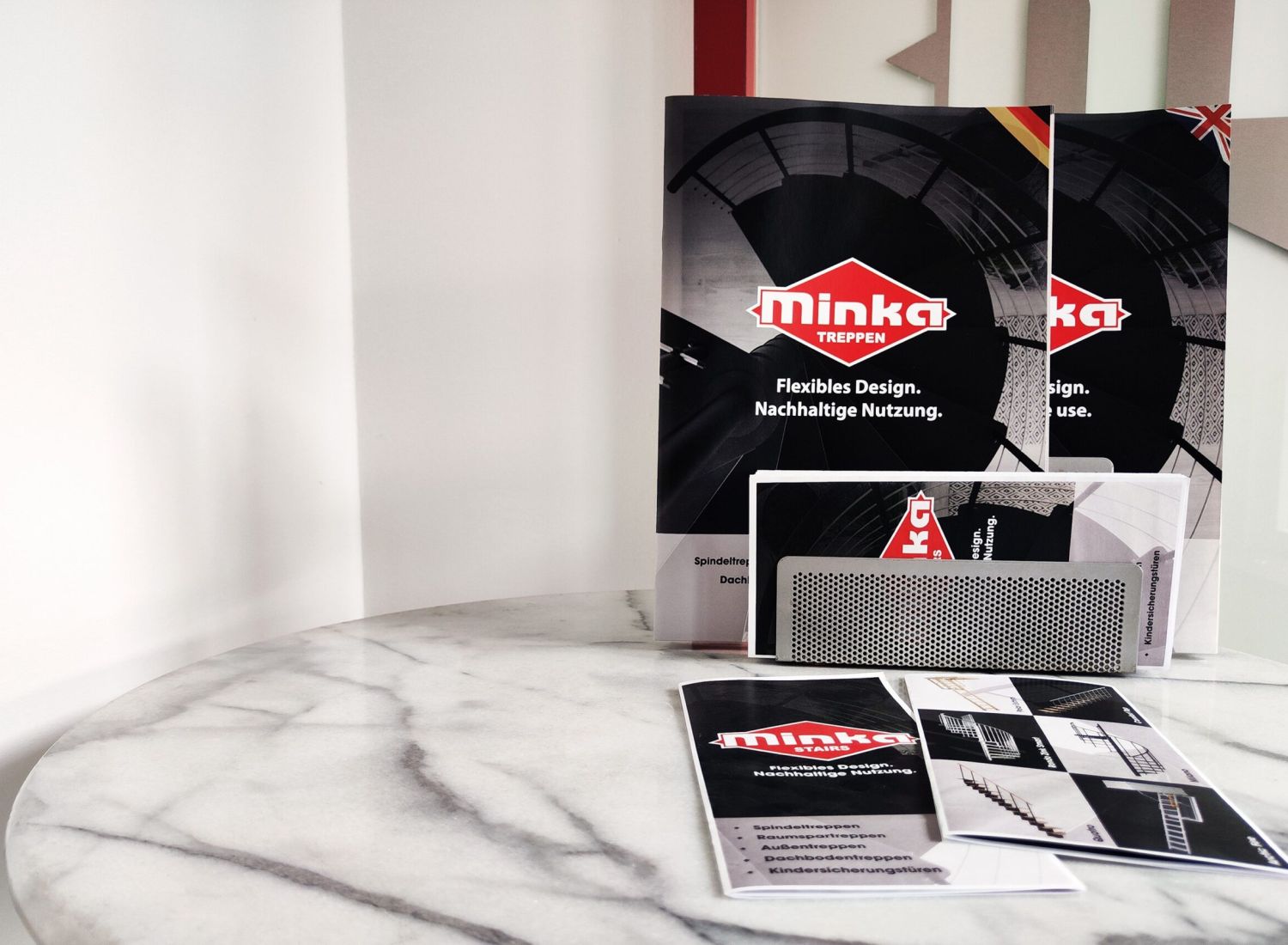 Downloads: Verschiedene Informationsmaterialien und Broschüren der Firma Minka Treppen auf einem runden Marmortisch ausgelegt.