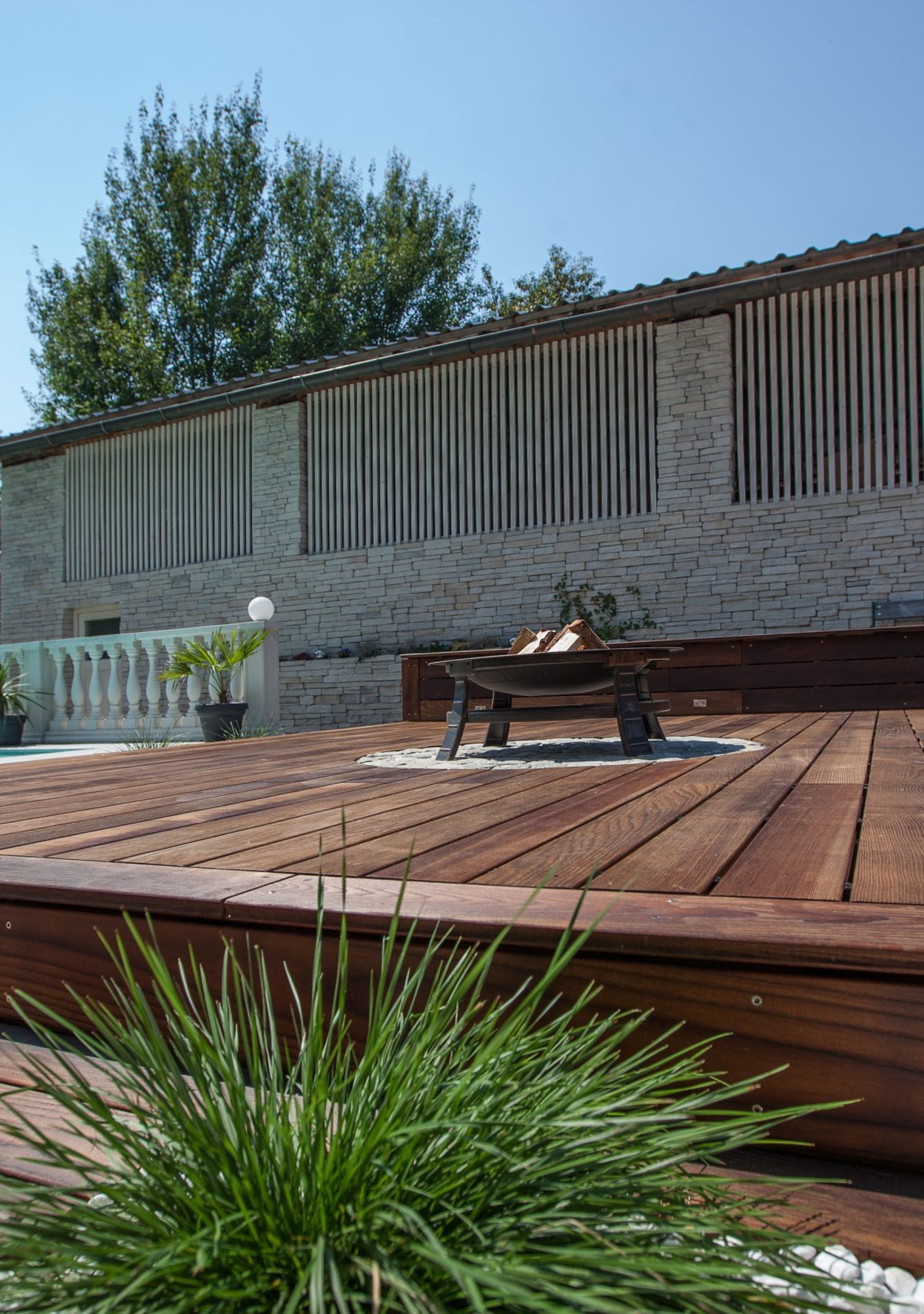 Elegante Terrasse aus Minka Wood Lotus mit eingelassener Feuerstelle und integriertem Sitzbereich, neben einem Pool und dekorativen Pflanzgefäßen.