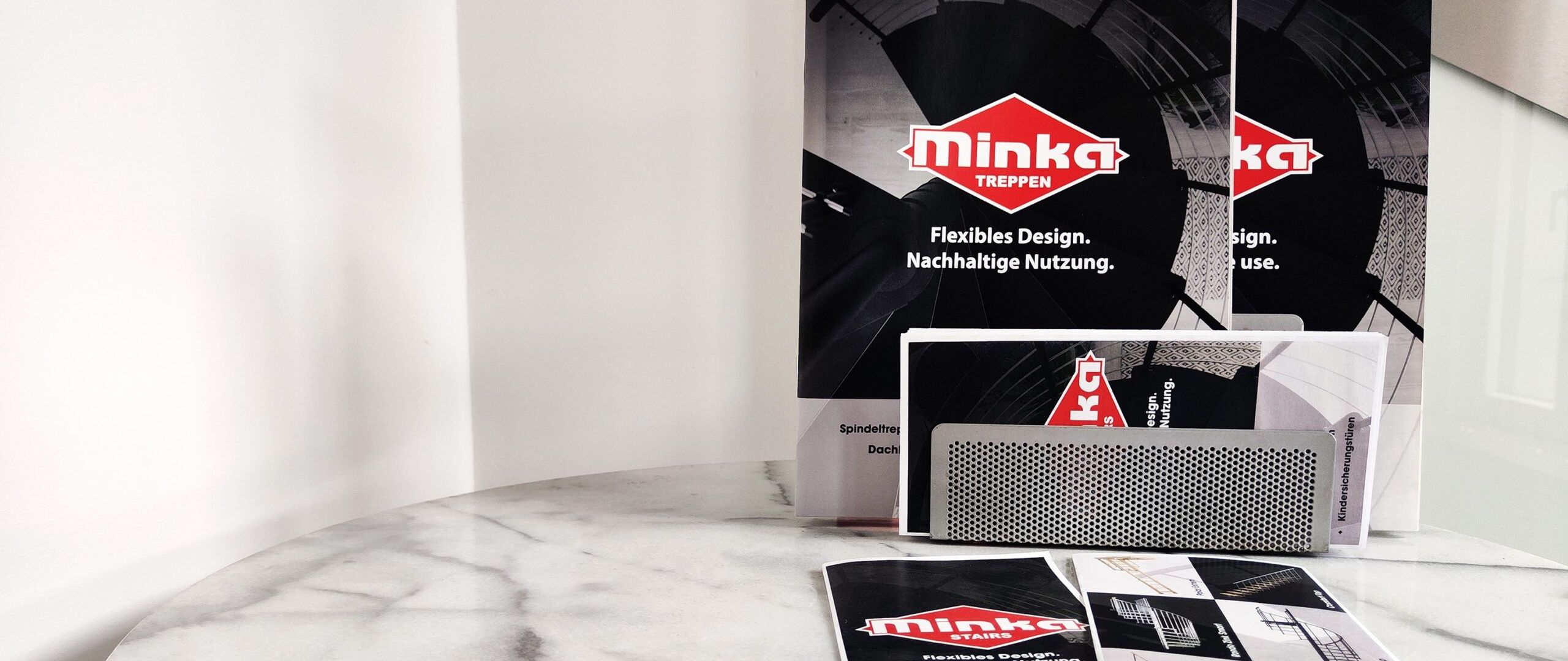 Downloads: Verschiedene Informationsmaterialien und Broschüren der Firma Minka Treppen auf einem runden Marmortisch ausgelegt.