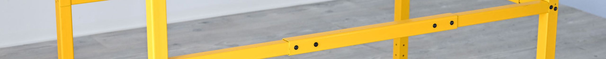 Gelbes Minka Lukenschutzgeländer aus Metall, rechteckige Umrahmung zur Absturzsicherung an Deckenöffnungen, montiert auf einem hellen Holzboden.