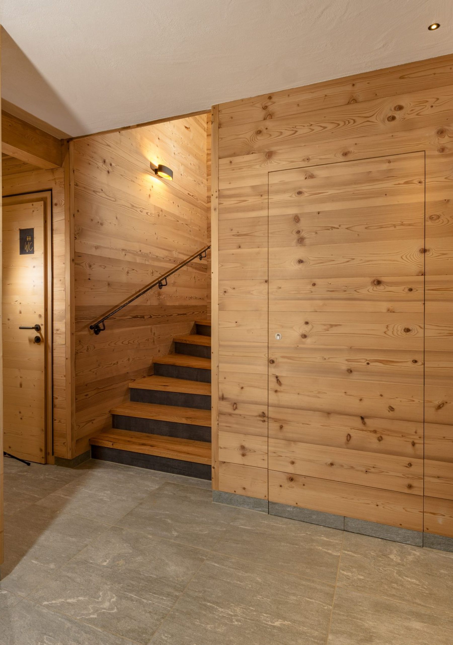 Innenbereich mit Wand- und Türelementen aus Gladiola-Holzpaneelen, gebürstet. Die warmen Holzpaneele kombiniert mit Natursteinboden und moderner Beleuchtung schaffen eine gemütliche und elegante Atmosphäre im Almwelt Schwab-Walcher.