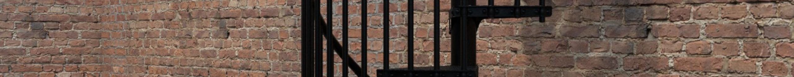 Außenspindeltreppe Rondo Zink Color in Schwarz vor einer Backsteinfassade. Die Treppe aus feuerverzinktem Stahl mit schwarzer Pulverbeschichtung verfügt über senkrechte Stäbe und Tränenblech-Stufen für sicheren Tritt im Außenbereich.