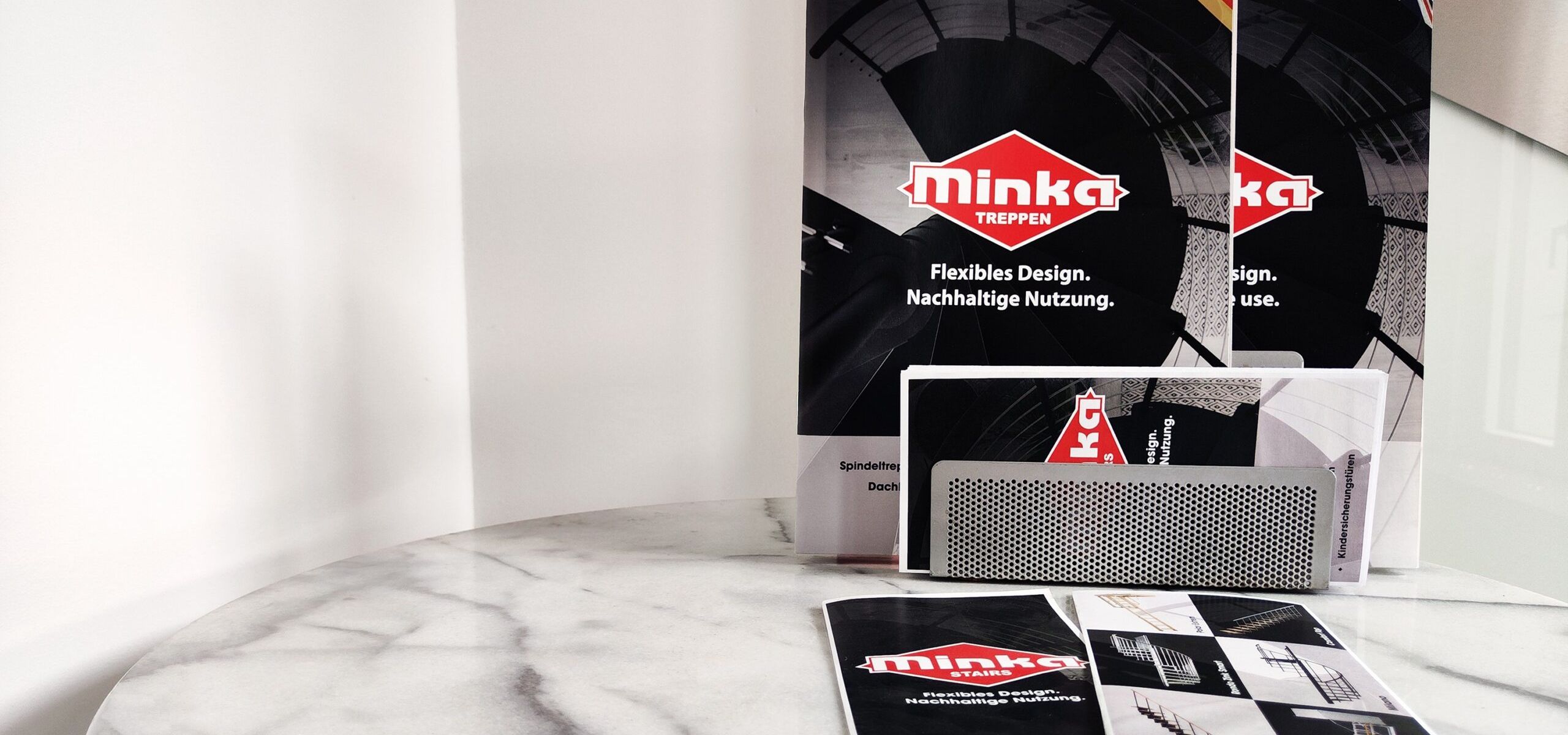 Downloads: Verschiedene Informationsmaterialien und Broschüren der Firma Minka Treppen auf einem runden Marmortisch ausgelegt.
