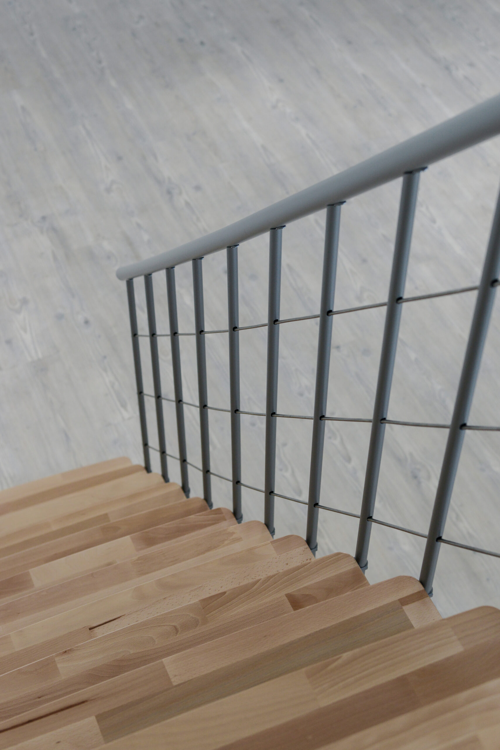 Nahaufnahme der Comfort Top Treppe aus der oberen Perspektive. Die Buchenholzstufen zeigen eine natürliche Maserung und sind mit einem modernen grauen Metallgeländer kombiniert.