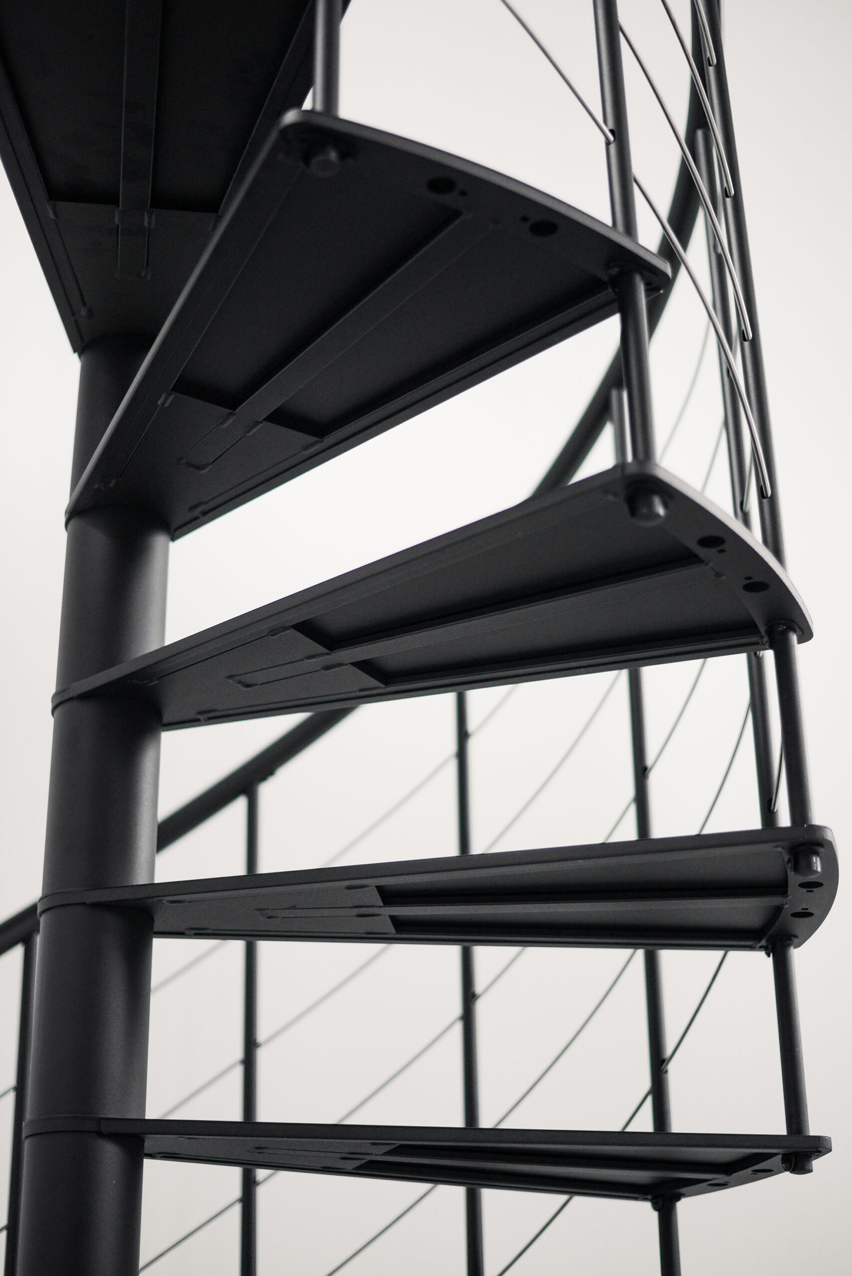 Detailaufnahme der Spindeltreppe „Milano“ aus Metall mit schwarzen, dreieckigen Trittstufen und einem umlaufenden Geländer aus vertikalen Stäben und horizontalen Untergurten.