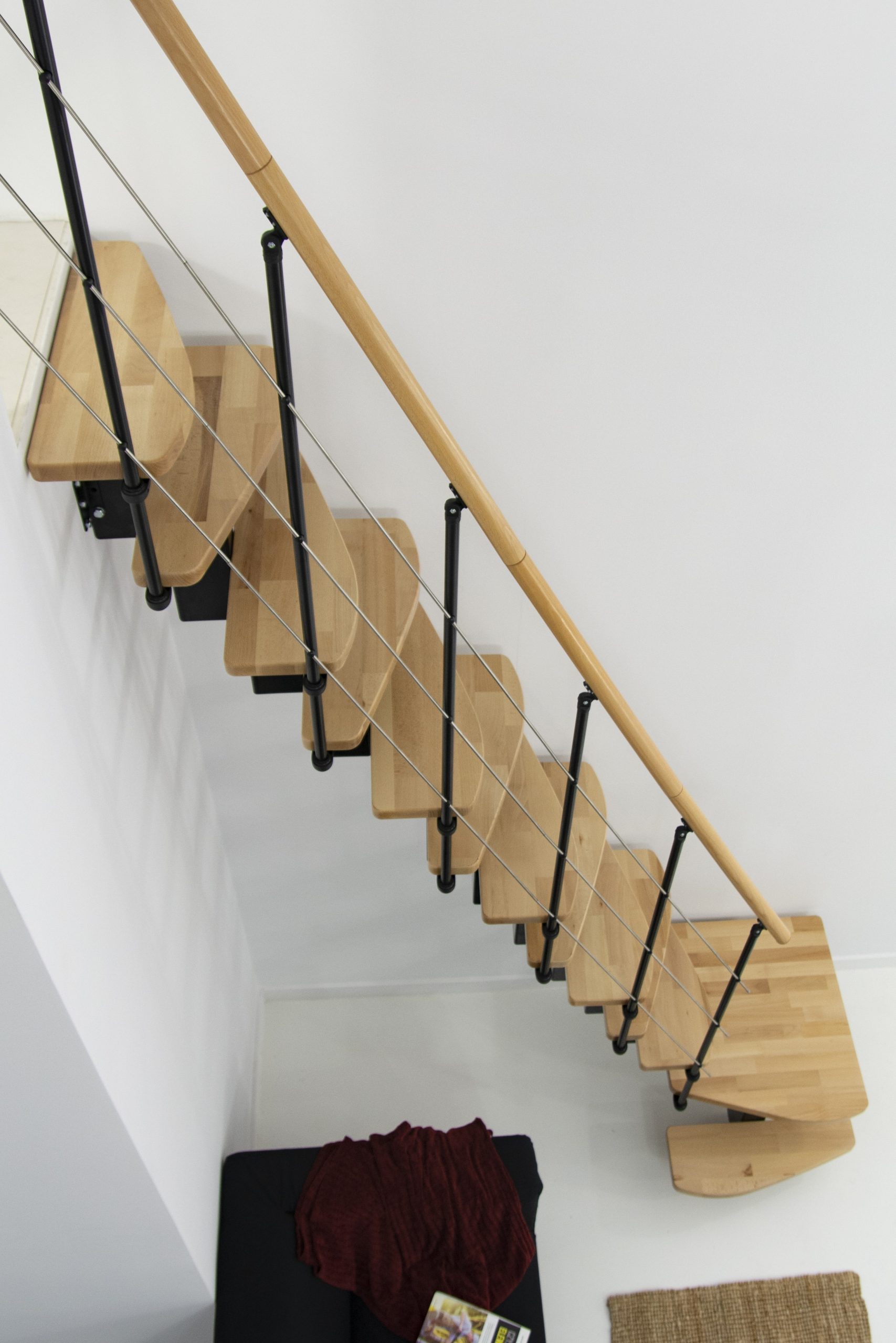 Mittelholmtreppe Quatro Turn mit 1/4 gewendelten Buchenstufen, schwarzem Metallgeländer mit Untergurten und Holzhandlauf, von oben aufgenommen.