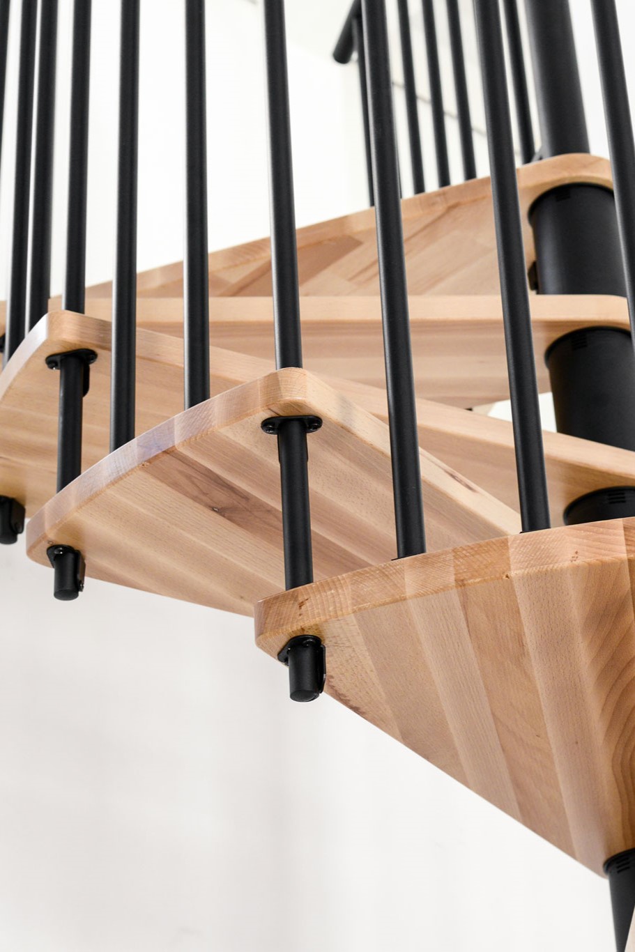 Nahaufnahme der Buchenstufen und des schwarzen Metallgeländers der Spindeltreppe Spiral Wood, montiert in einem hellen Raum.