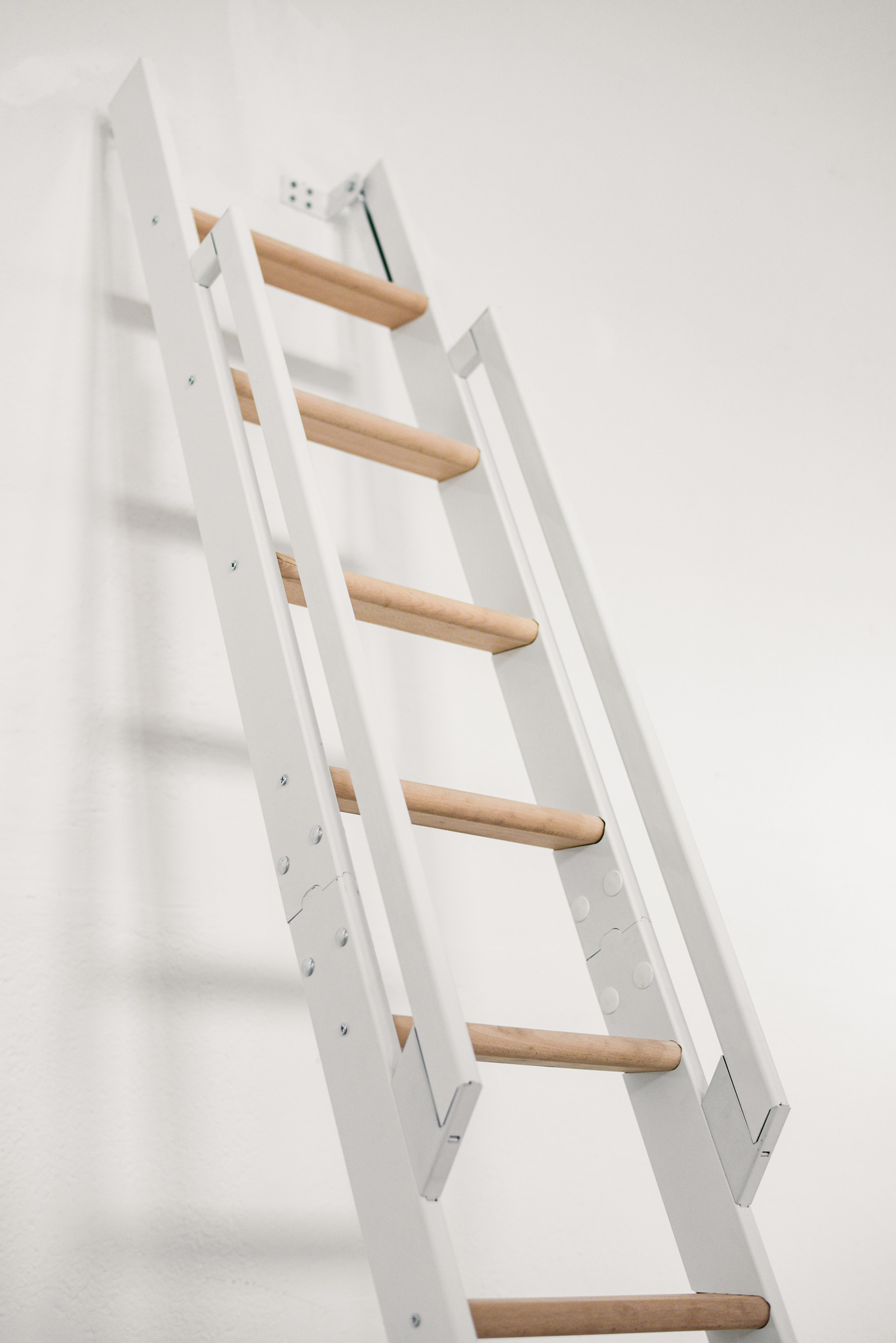 Detailansicht der Raumspartreppe Strong mit weißem Gestell und Trittstufen aus Buche. Sichtbar ist das beidseitige Geländer mit seitlich verschraubten Holmelementen.