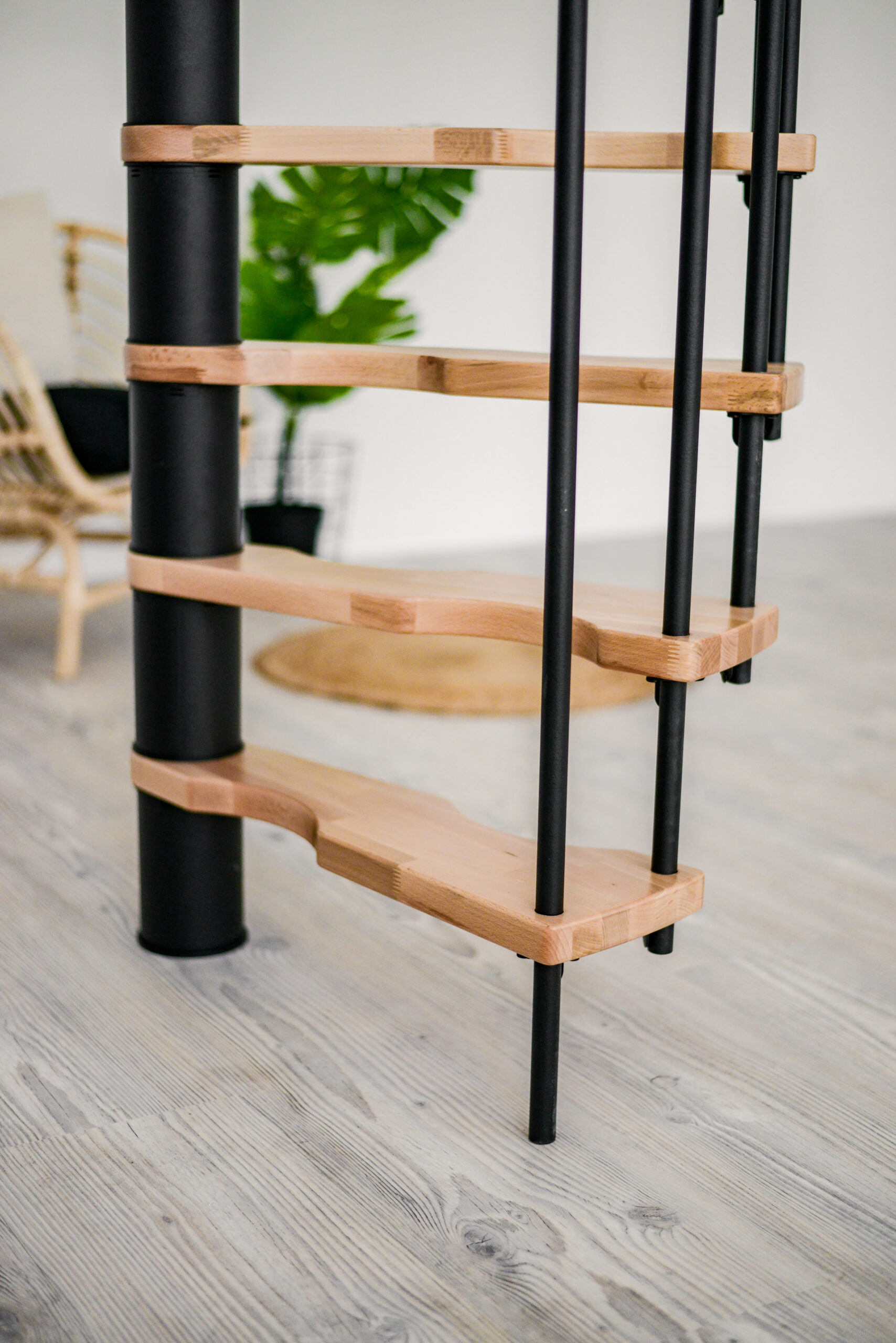 Nahaufnahme der unteren Stufen der Spindeltreppe Suono. Die Kombination aus schwarzen Geländerstäben und hellen Holzstufen sorgt für ein modernes und stabiles Erscheinungsbild.
