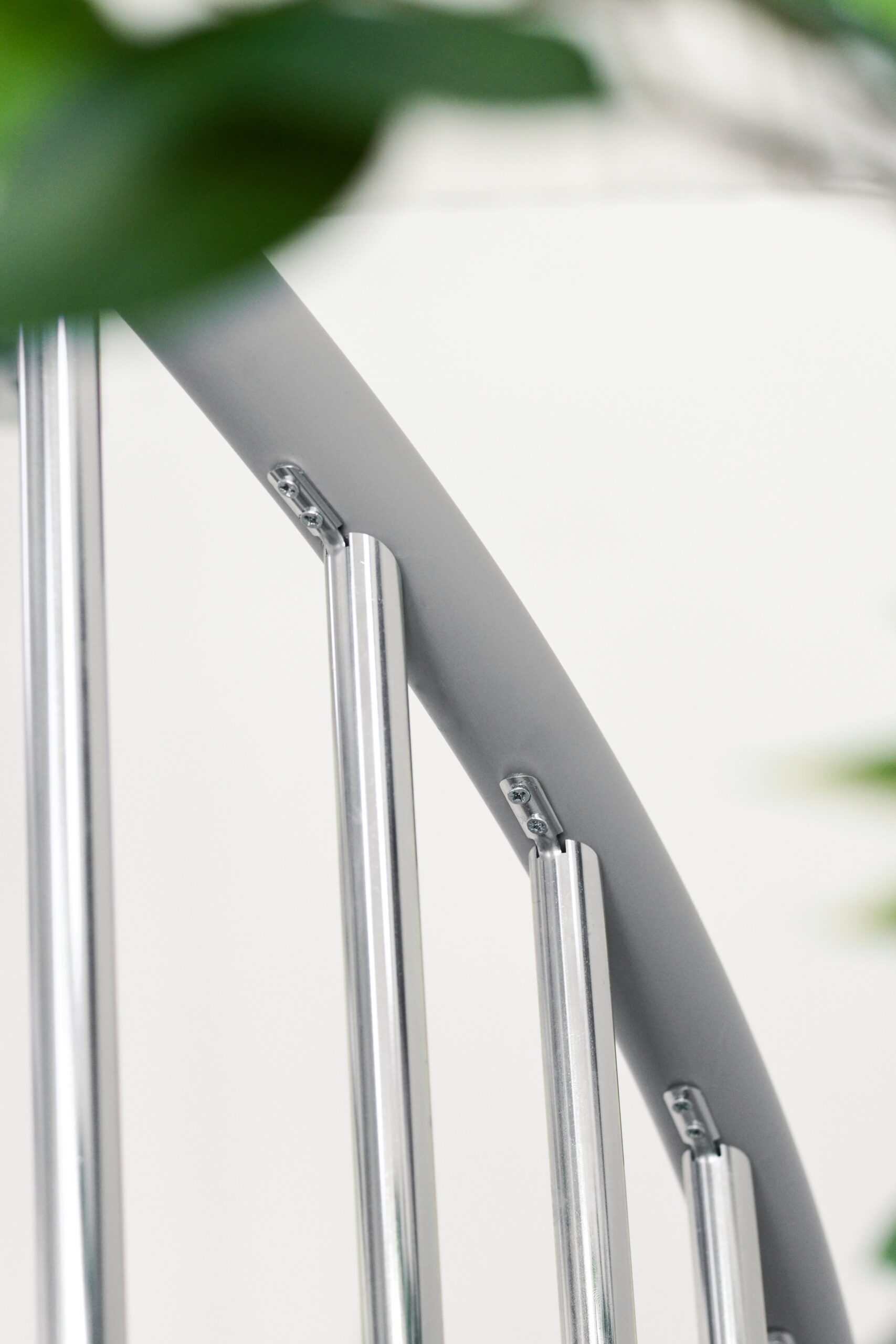 Detailaufnahme des Geländers der Außenspindeltreppe Rondo Zink Smart. Zu sehen ist die Befestigung der senkrechten Metallstäbe am gebogenen Handlauf aus PVC. Im Vordergrund unscharfe grüne Blätter.