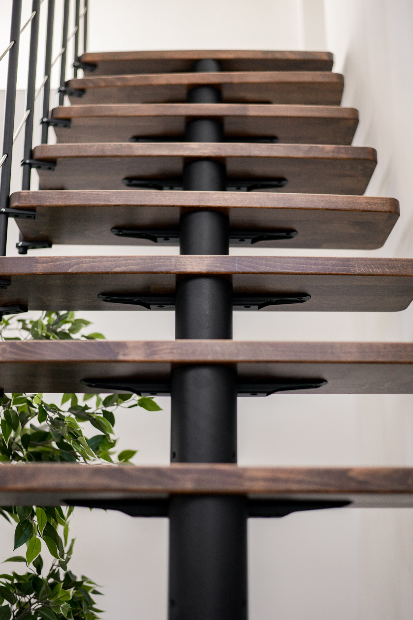 Detailansicht einer Comfort Top Turn Treppe im Walnuss-Schwarz-Design. Die dunkel gebeizten Holzstufen in Walnussoptik sind auf einer schwarzen Metall-Mittelholmkonstruktion befestigt.