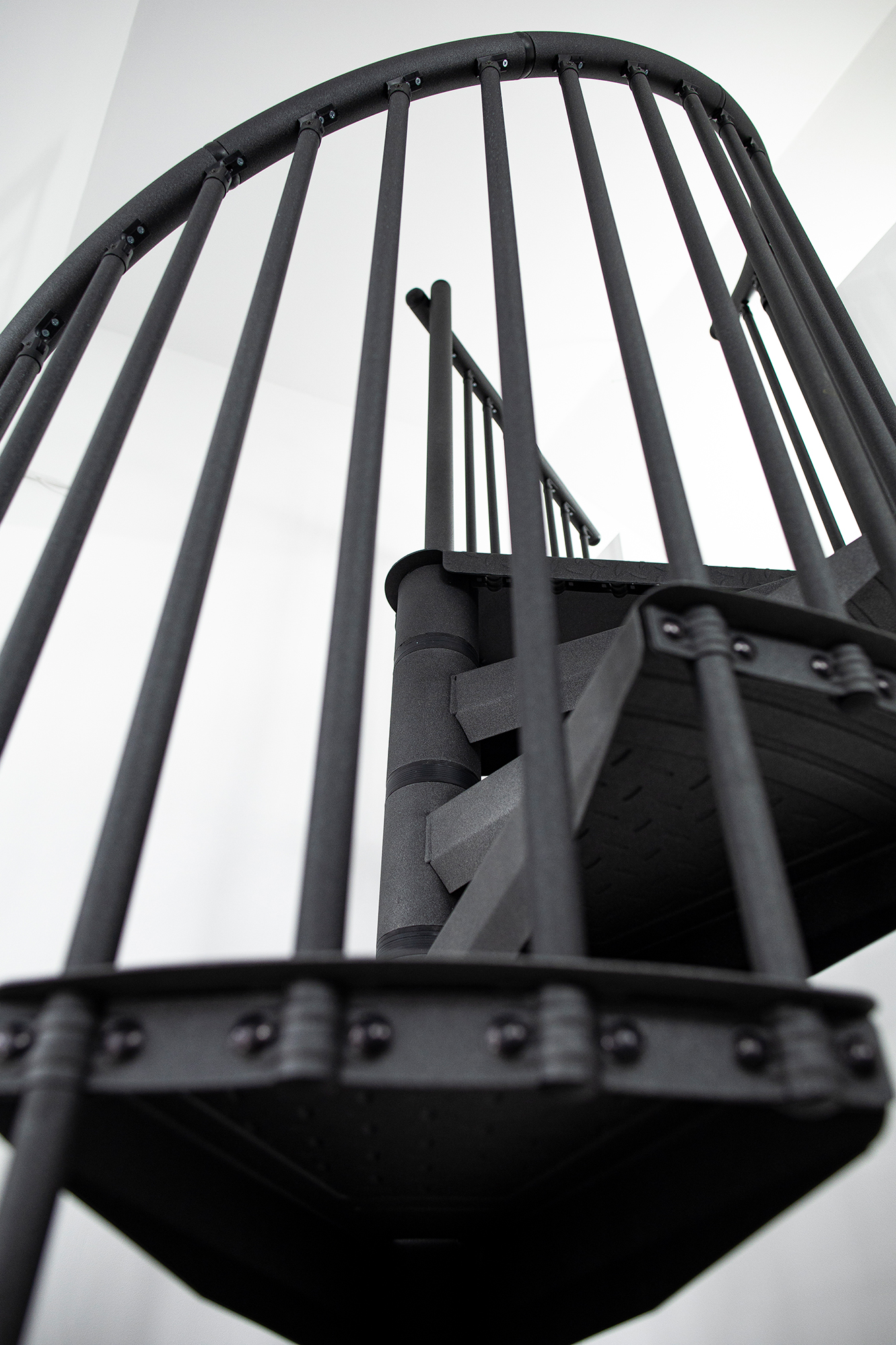 Detailansicht der Spindeltreppe Rondo Color in Anthrazit von unten. Im Fokus steht das senkrechte Stabgeländer aus pulverbeschichtetem Metall sowie die strukturierte Oberfläche der Stufen mit rutschhemmender Tränenblech-Optik.