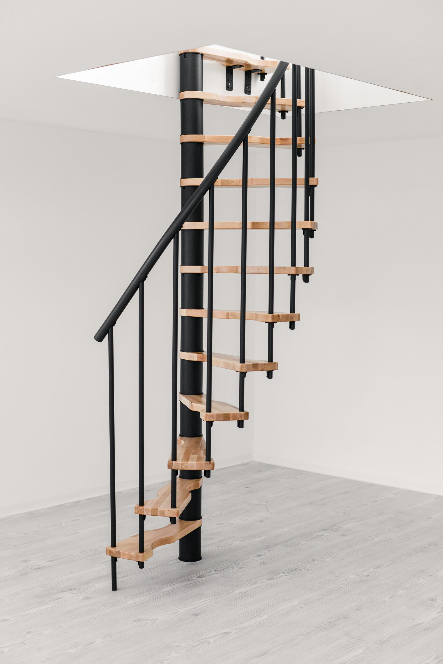 Die Spindeltreppe Suono Smart besticht durch ihr platzsparendes Design mit schwarzem Mittelrohr, schwarzen Geländerstäben und hellen Holzstufen – ideal für minimalistische Wohnräume.