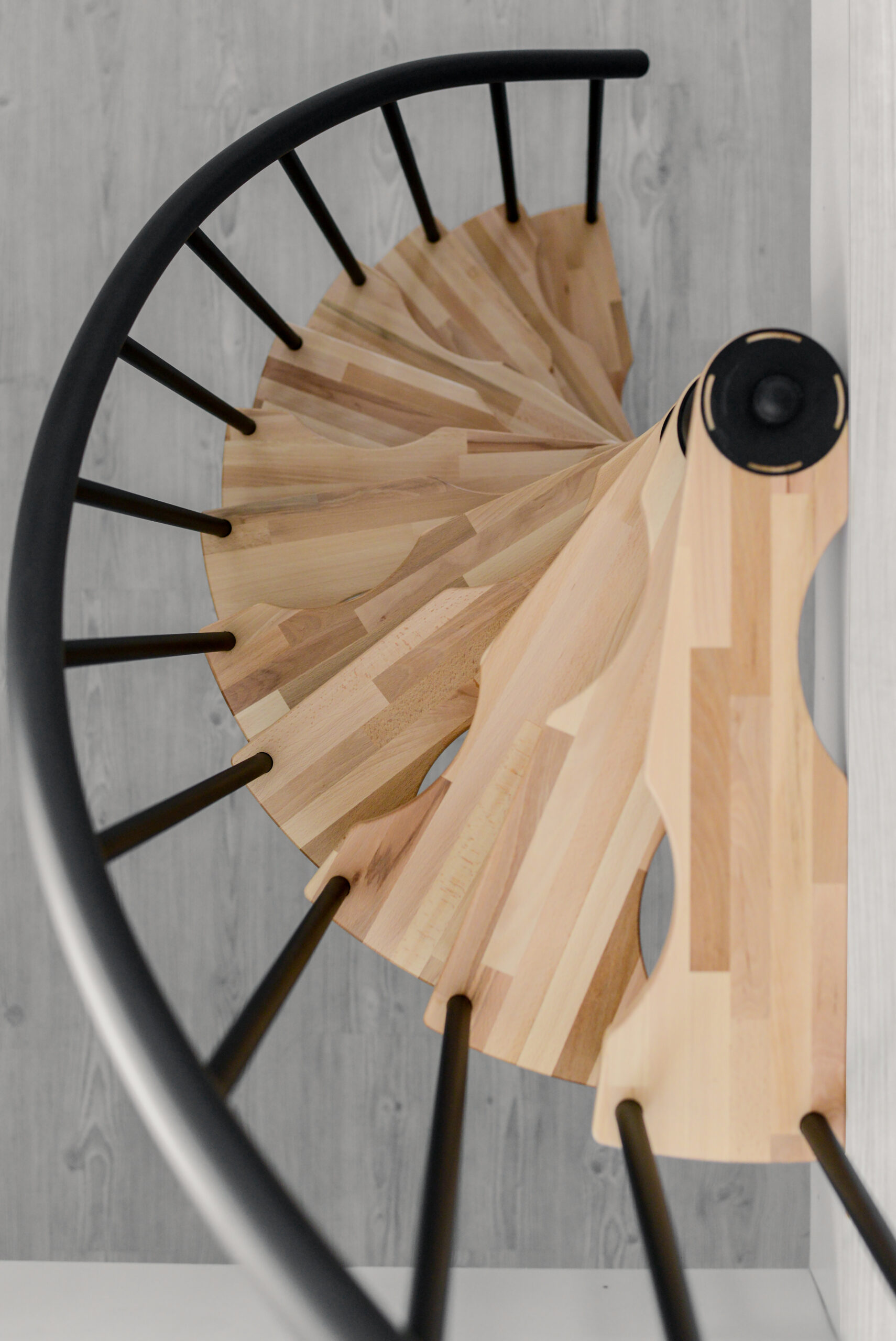 Blick von oben auf die Spindeltreppe Suono Smart. Die spiralförmig angeordneten Holzstufen und das schwarze Geländer zeigen das elegante und platzsparende Design der Treppe.