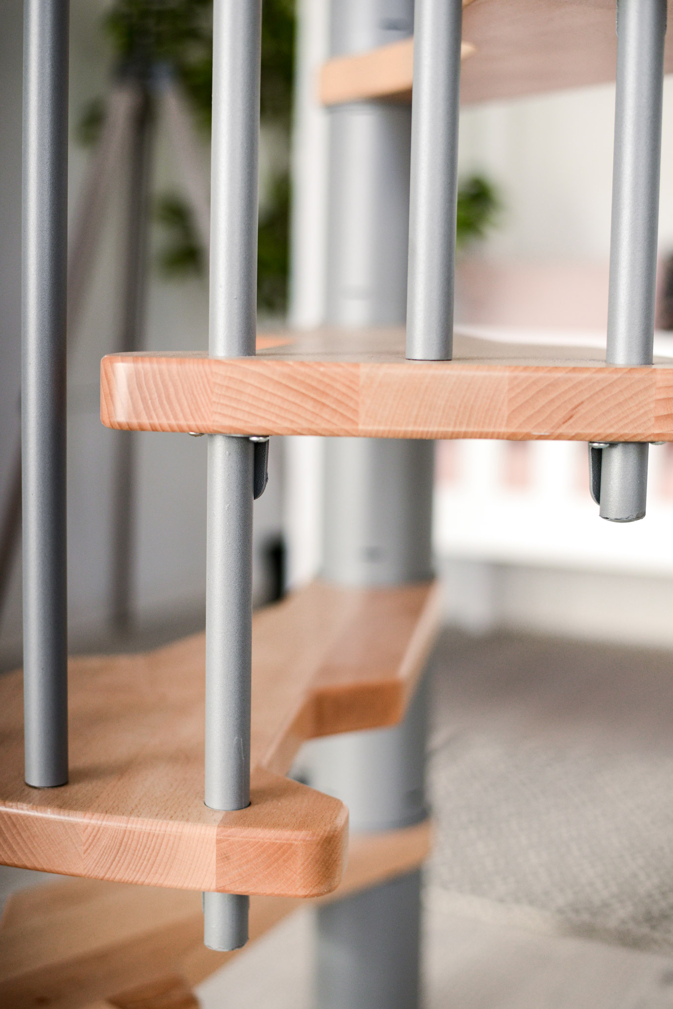 Nahaufnahme der Stufen der Spindeltreppe Metallica. Die Verbindung von grauem Metallgeländer und hellen Holzstufen sorgt für ein modernes und stabiles Design.