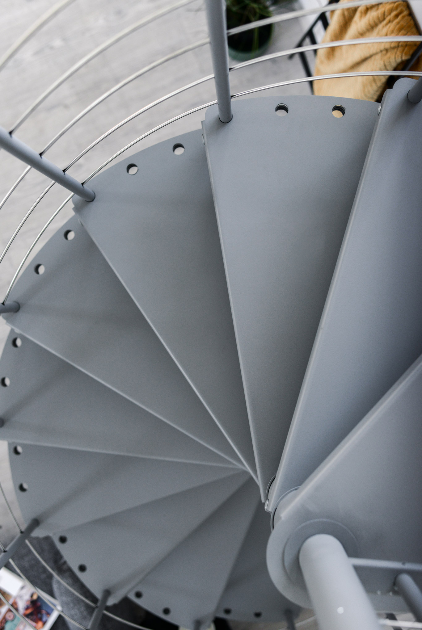 Obere Ansicht der grauen Spindeltreppe aus Metall Spino Smart. Die dreieckigen Stufen drehen sich spiralförmig um eine zentrale Säule. Außen verläuft ein Metallgeländer mit waagerechten Edelstahluntergurten.