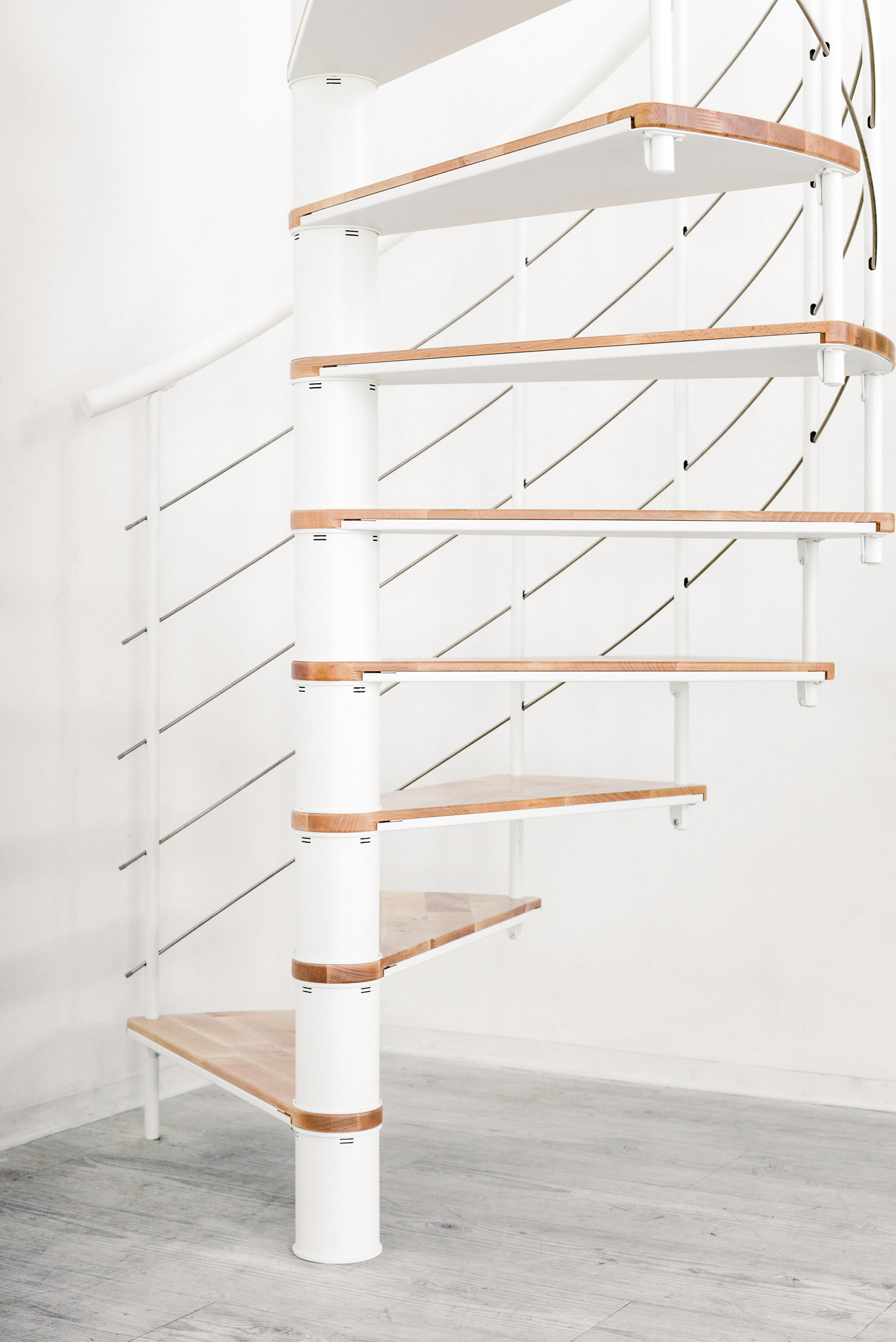Detailaufnahme der Spindeltreppe Fusion, Ansicht seitlich auf die weiße Spindel, die Buchenstufen mit Metallaufschüben und das Geländer mit Edelstahl-Untergurten.