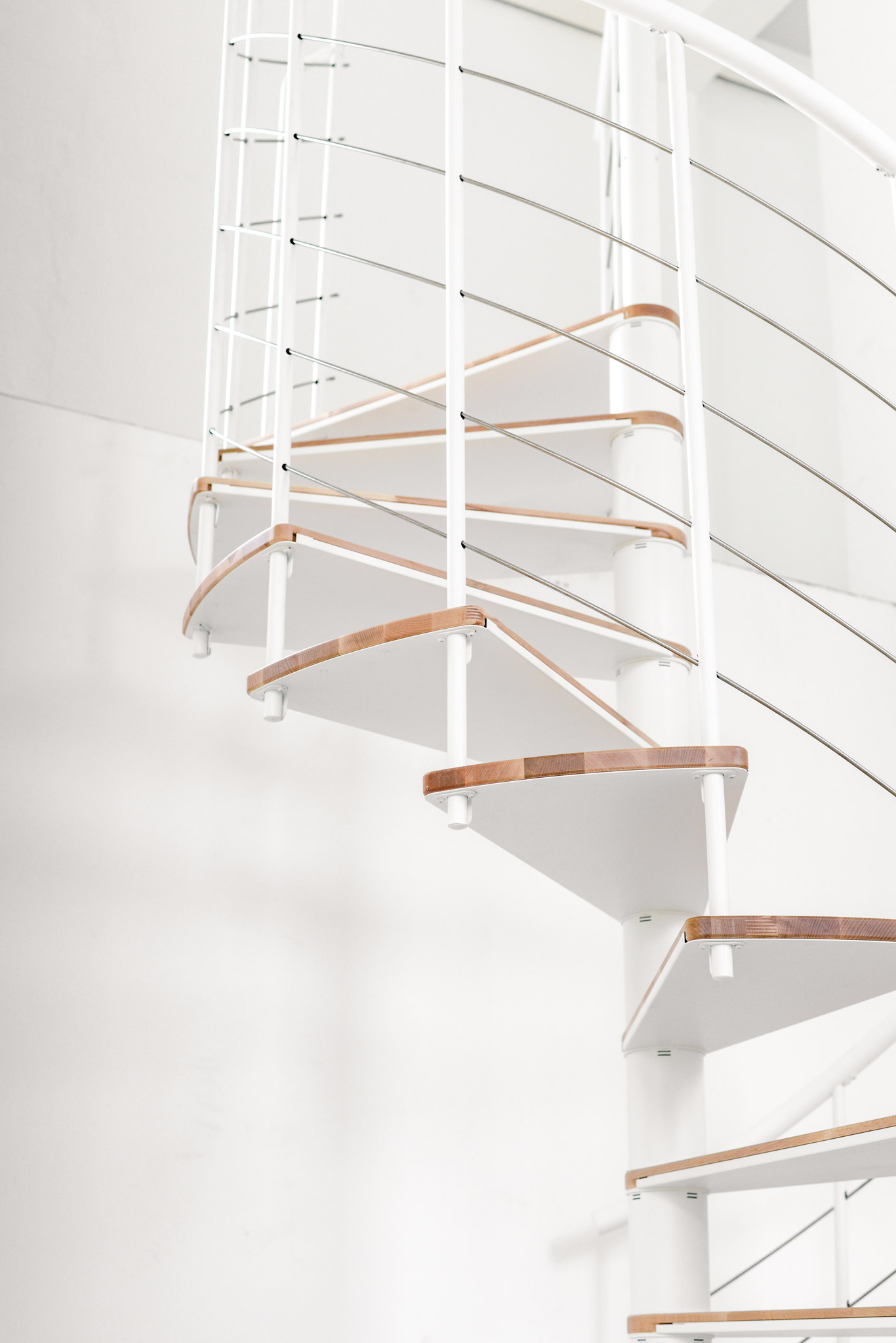 Detailaufnahme der Spindeltreppe Fusion, Ansicht von schräg unten auf die weißen Metallaufsätze unter den Buchenstufen.