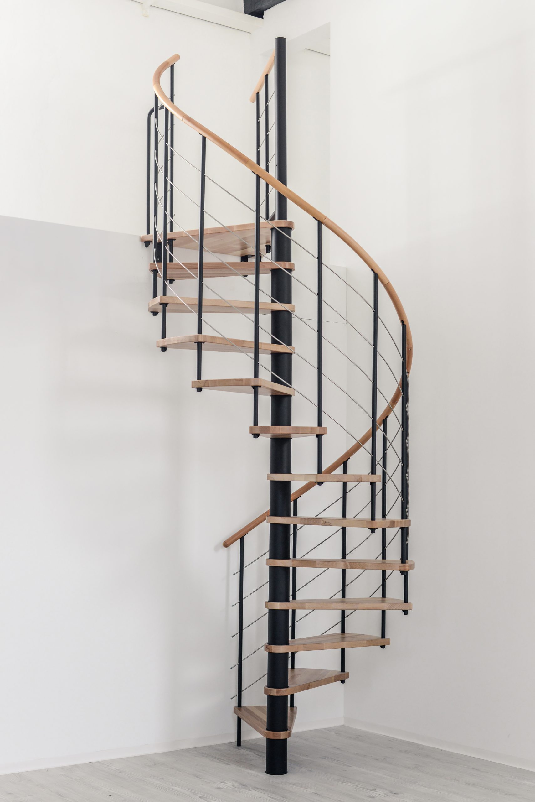 Spindeltreppe Venezia mit Stufen und Handlauf in Buchenholz, schwarzen Metallteilen und Edelstahl-Untergurten, eingebaut in einen weißen Raum.