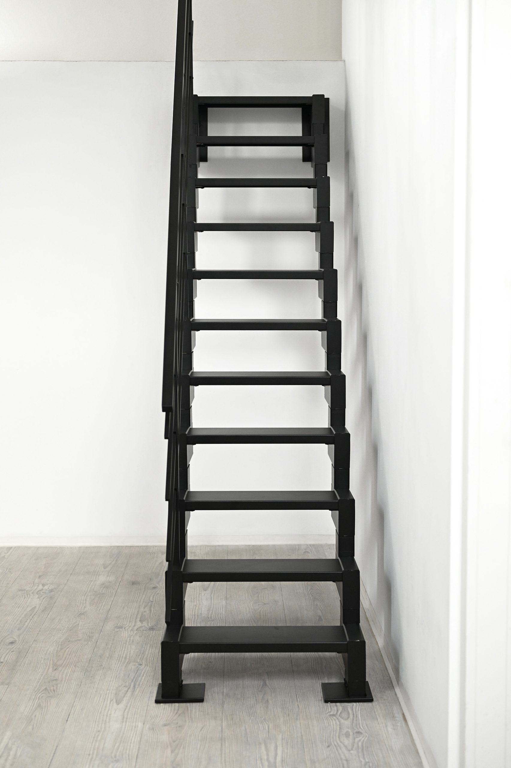 Frontale Ansicht der geradläufigen Raumspartreppe Modulario Mini in Schwarz. Die Treppe mit Metallstufen steht auf einem hellen Holzfußboden. Die schmalen Stufen sparen Platz und unterstreichen das moderne Design.