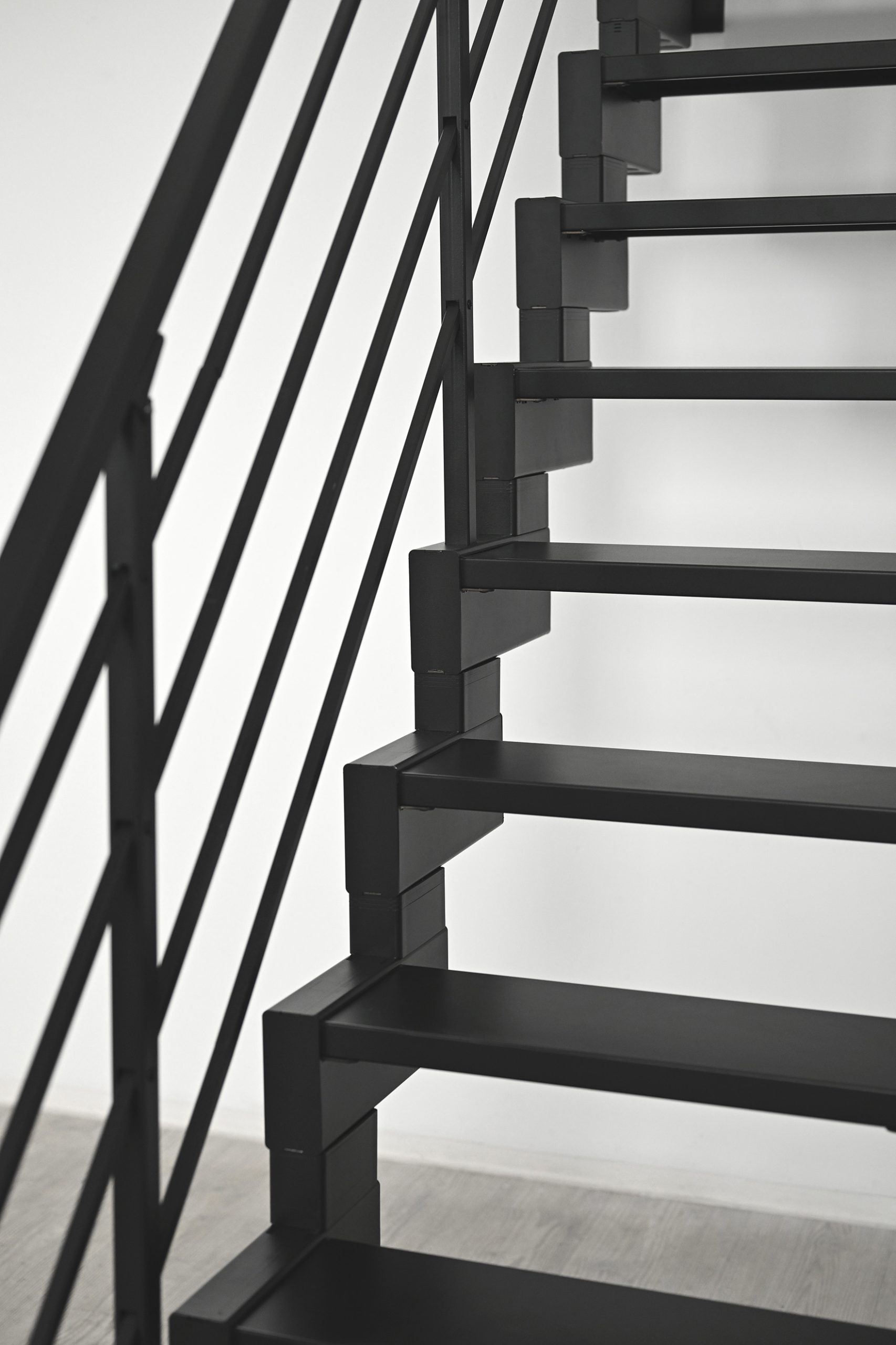Nahaufnahme der Modulario Mini Treppe in Schwarz. Sichtbar sind die rechteckigen Metallstufen mit versetzter Geometrie sowie das seitlich verlaufende Geländer mit horizontalen Stäben. Die Konstruktion wirkt modern und industriell.