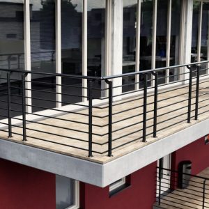 Modernes Brüstungsgeländer Orion-Top in Anthrazit auf einem großzügigen Balkon mit Holzbelag und Betonplatte. Die senkrechten Pfosten sind auf der Balkonfläche montiert und tragen waagerechte, gleichmäßig angeordnete Streben. Das Geländer unterstreicht den zeitgemäßen, klaren Architekturstil des Gebäudes.