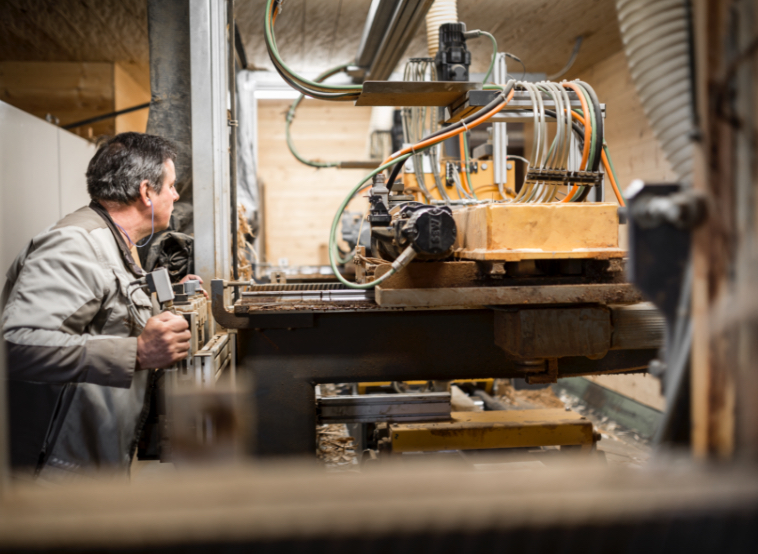 Arbeiter bedient eine Holzbearbeitungsmaschine mit Kabeln und Absaugung – Hacken von Holz.
