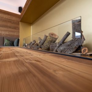 Detailaufnahme im Hotel Essigmanngut: stilvoller Innenbereich mit Wänden und Möbeln aus Azalea-Holz, gebürstet. Warme Maserung kombiniert mit modernen Elementen wie Glas und Kamin.