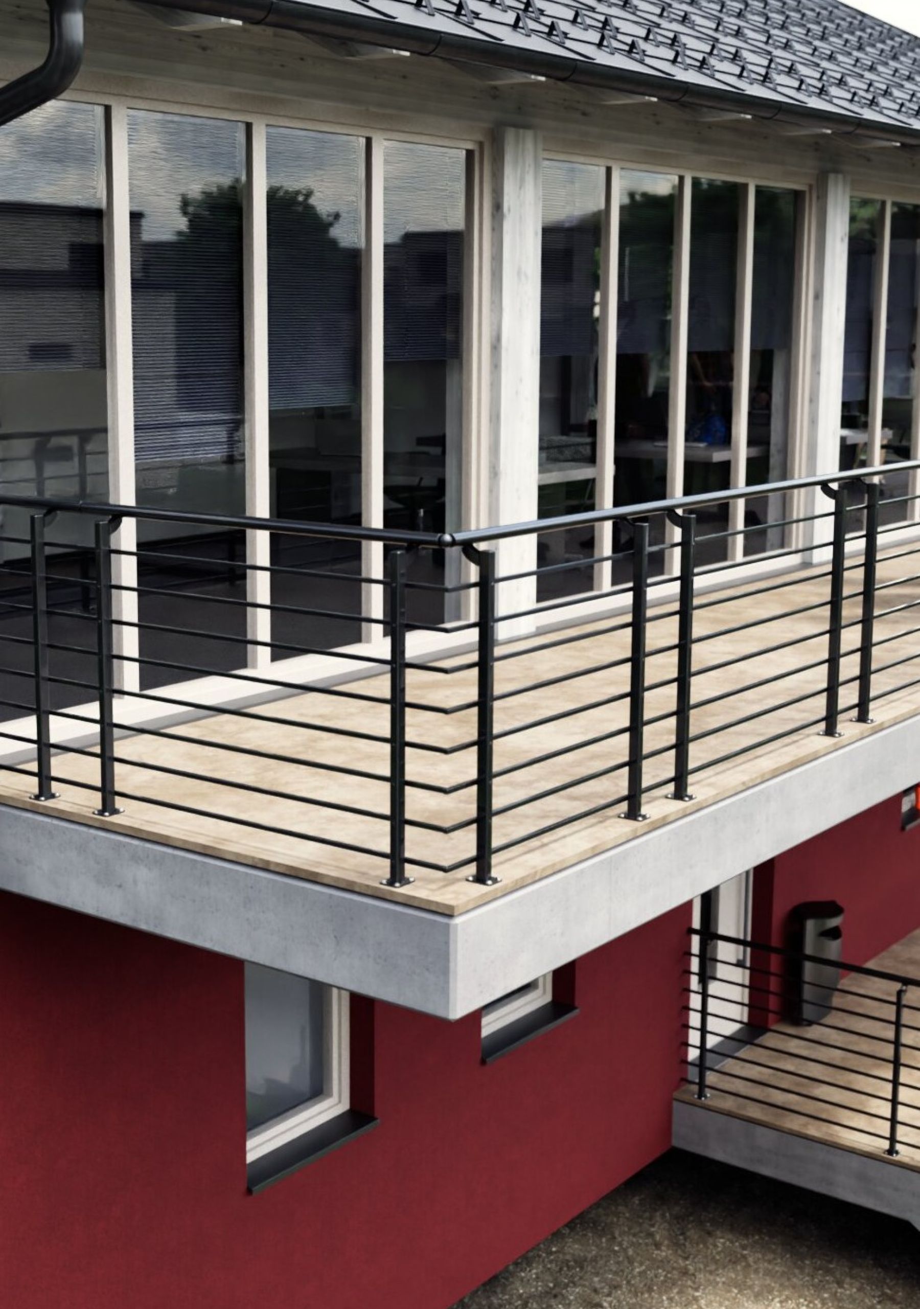 Modernes Brüstungsgeländer Orion-Top in Anthrazit auf einem großzügigen Balkon mit Holzbelag und Betonplatte. Die senkrechten Pfosten sind auf der Balkonfläche montiert und tragen waagerechte, gleichmäßig angeordnete Streben. Das Geländer unterstreicht den zeitgemäßen, klaren Architekturstil des Gebäudes.
