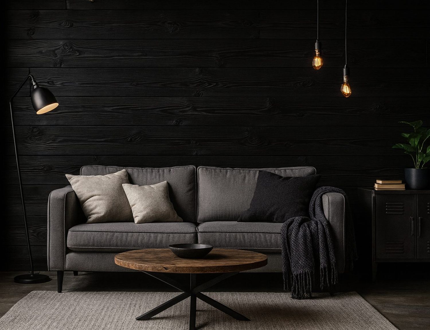 Dunkel gestalteter Wohnbereich mit grauem Sofa, runden Couchtisch aus Holz und Teppich, vor einer Wandverkleidung aus horizontal verlegten, schwarz gefärbten Holzbohlen, akzentuiert durch Stehleuchte, hängende Glühbirnen und dezente Dekoration.